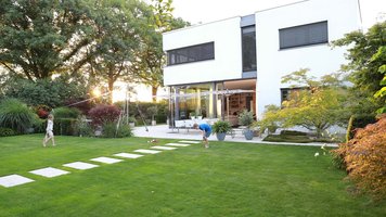Designergarten mit gepflegtem Rasen und weißem Haus