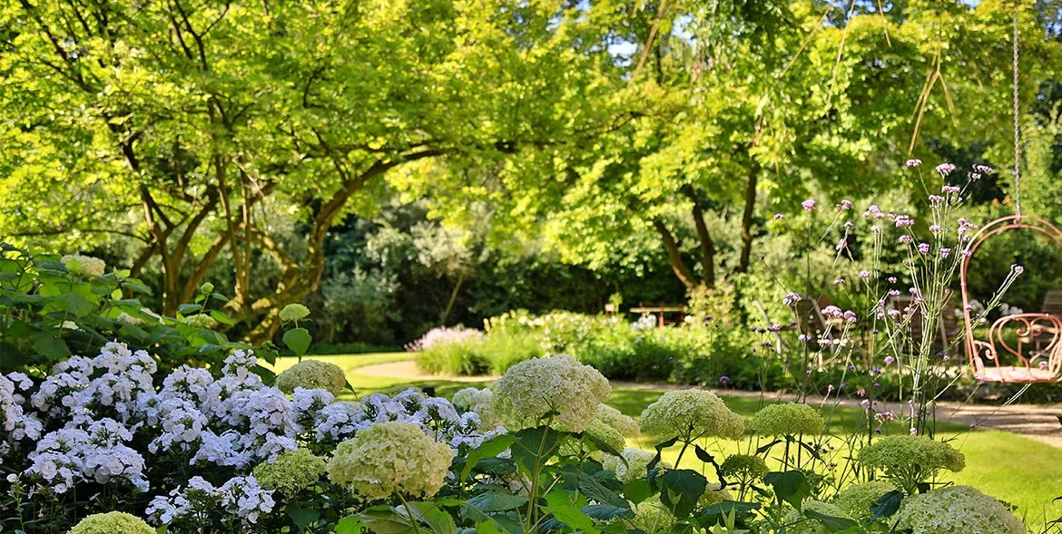Großer, grüner Garten mit vielen Blumen, Bäumen und Pflanzen.